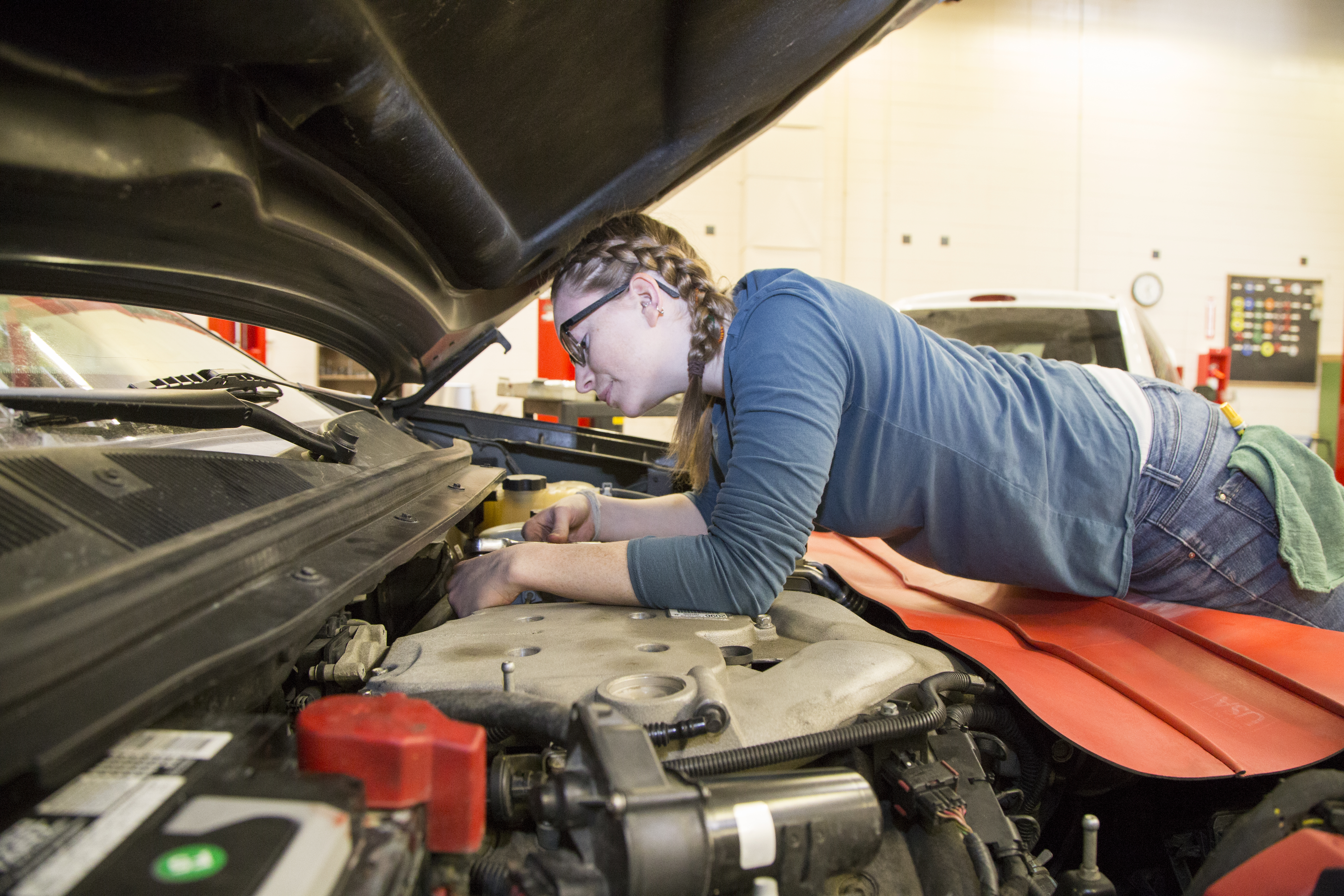A woman works under the hood of a car