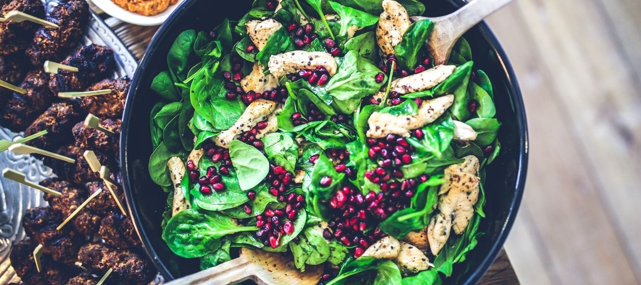 Spinach, chicken, and pomegranate seeds in a skillet