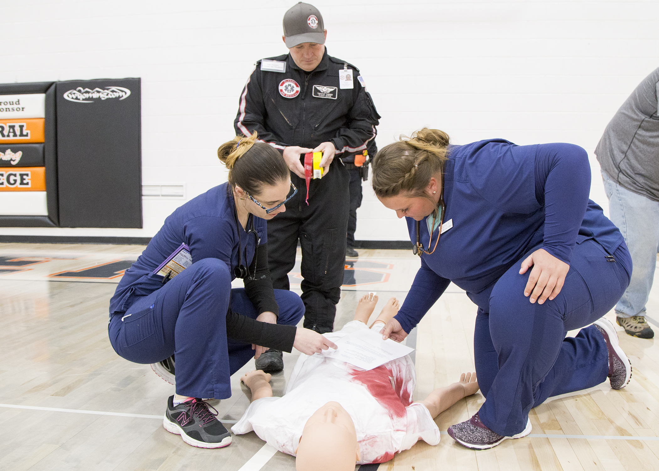 two nursing students look at a dummy for fake injuries while a flight for life medic assesses their work