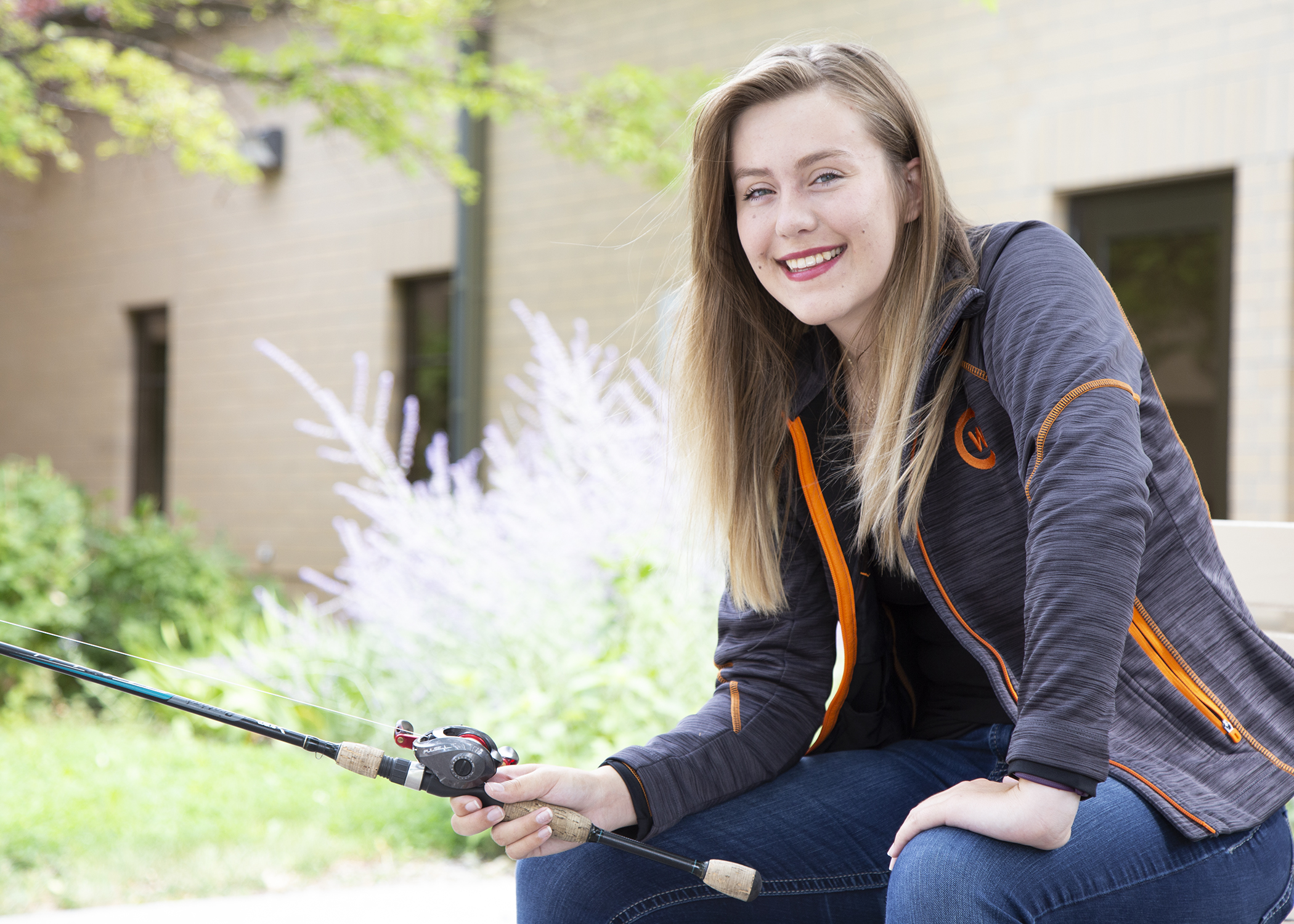 student Katy Carey sits on a bench with her fishing pole in hand