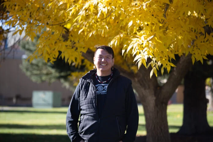 Picture of student Ray Youngchief with yellow colorful leaves on a tree behind him