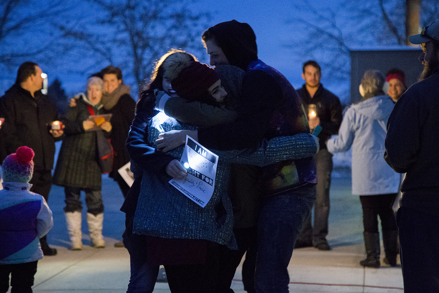 students hug at Ghostlight Project at dusk with flashlights in hand